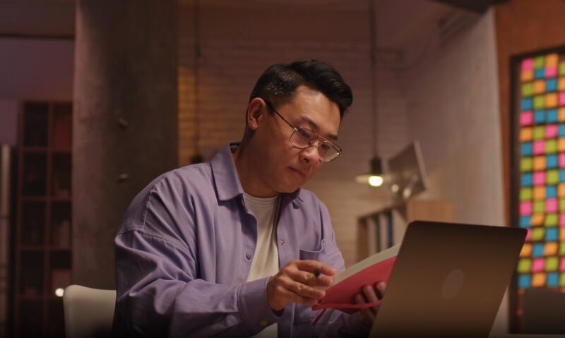 Man reads a book with laptop on a table